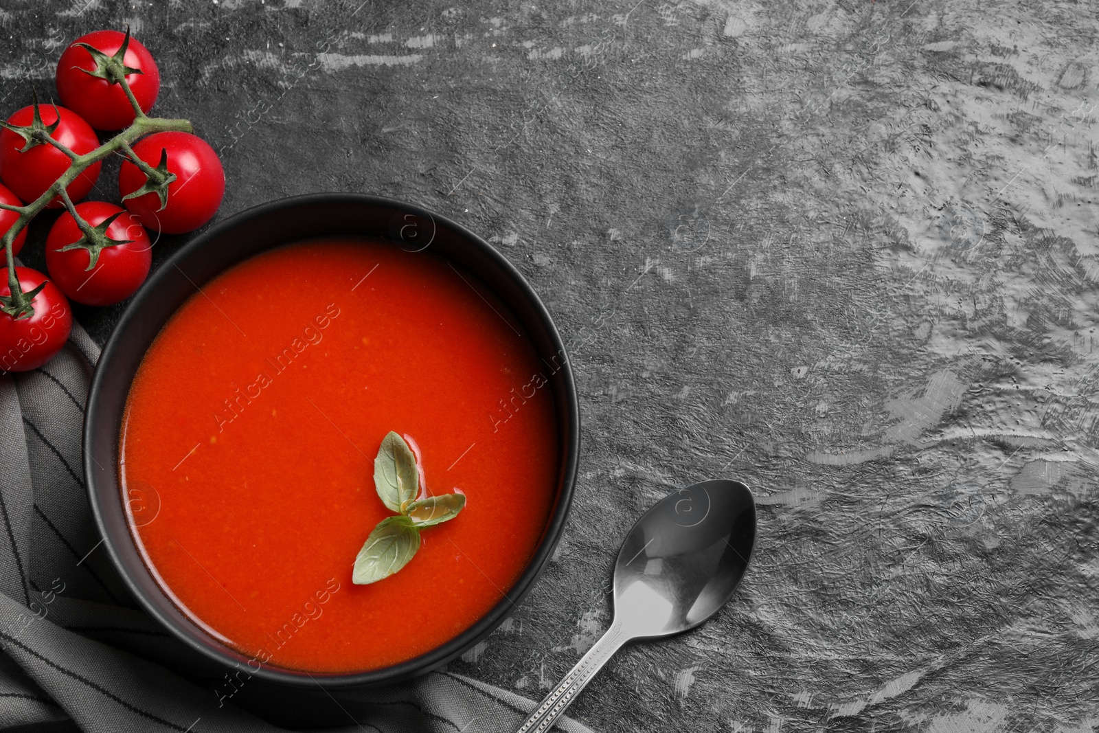 Photo of Delicious tomato cream soup in bowl served on dark textured table, flat lay. Space for text