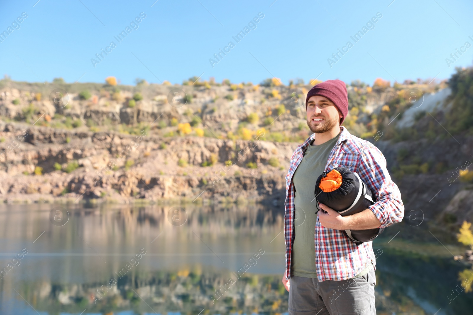 Photo of Male camper with sleeping bag near beautiful lake. Space for text