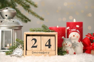 Photo of December 24 - Christmas Eve. Wooden block calendar, pocket watch and festive decor on snow against blurred lights