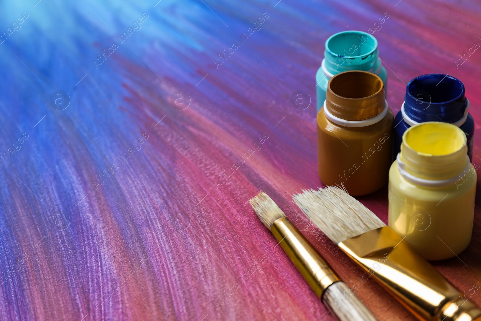 Photo of Jars with paints and brushes on abstract picture, closeup. Space for text