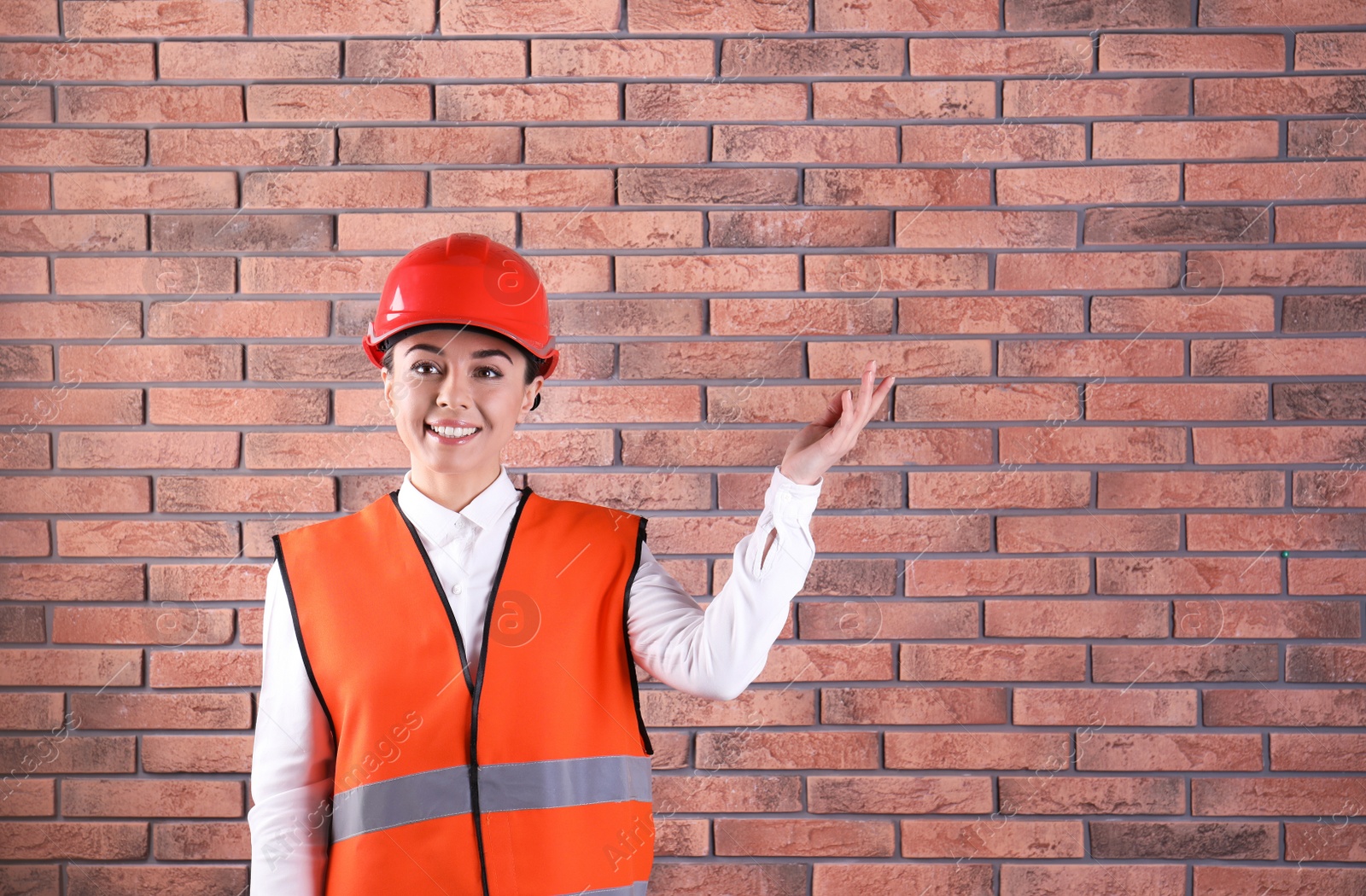 Photo of Female industrial engineer in uniform on brick wall background, space for text. Safety equipment