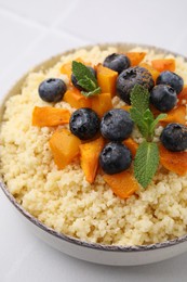 Photo of Bowl of tasty couscous with blueberries, pumpkin and mint on table, closeup