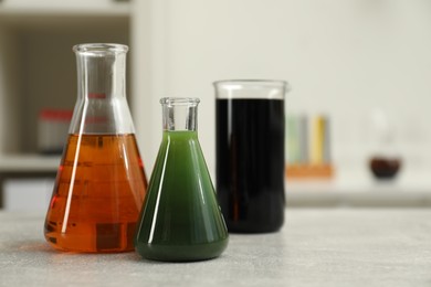 Photo of Flasks and beaker with different types of crude oil on light grey table, space for text