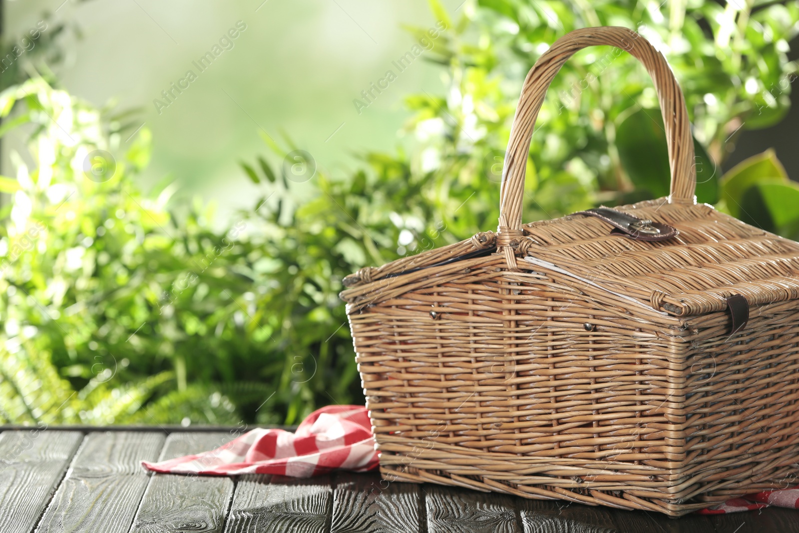 Photo of Closed wicker picnic basket on wooden table against blurred background, space for text