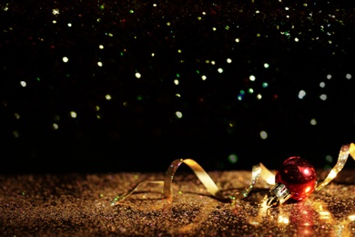 Photo of Golden glitter, Christmas ball and streamer against black background. Space for text