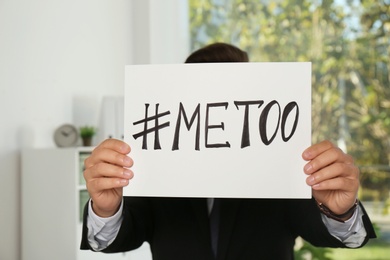 Photo of Man holding paper with text "#METOO" in office. Problem of sexual harassment at work