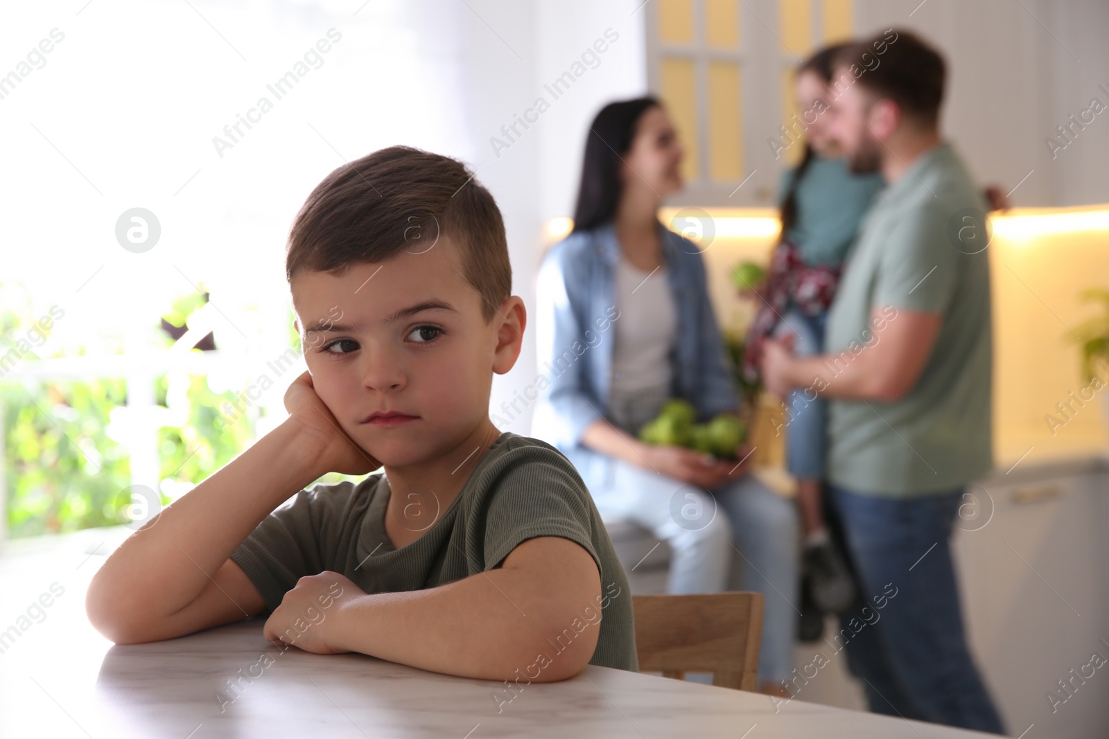 Photo of Unhappy little boy feeling jealous while parents spending time with his sister at home