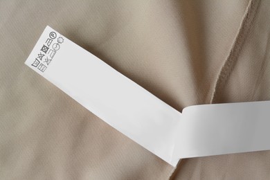 White clothing label with care information on beige garment, top view