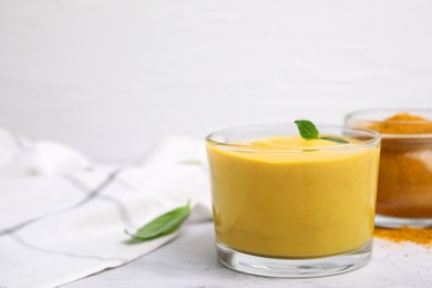 Tasty curry sauce, powder and basil leaves on white table, closeup. Space for text