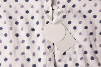 Photo of Blank tags on white shirt with polka dot pattern, top view. Space for text