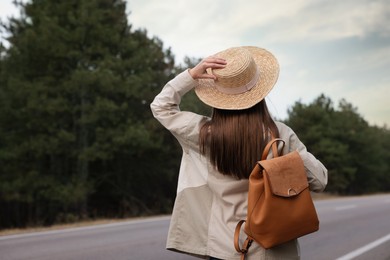 Photo of Young woman with stylish backpack on empty road in forest, back view. Space for text