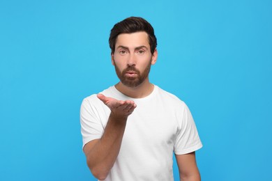 Photo of Handsome man blowing kiss on light blue background
