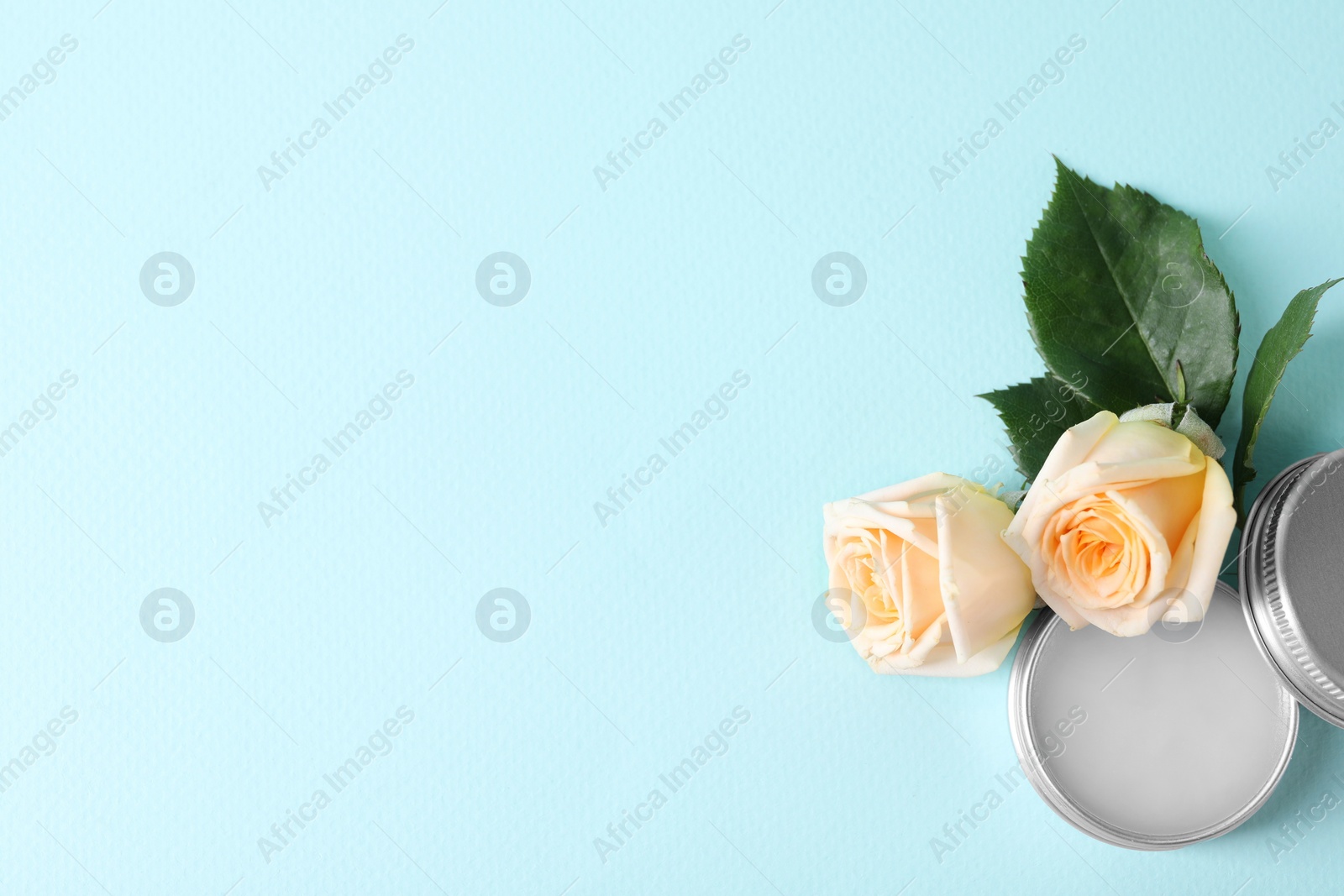 Photo of Lip balm and rose flowers on light blue background, top view. Space for text