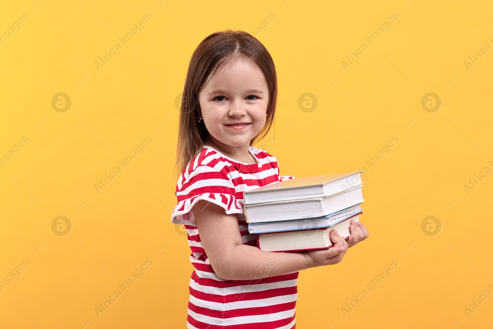 Photo of Cute little girl with books against orange background