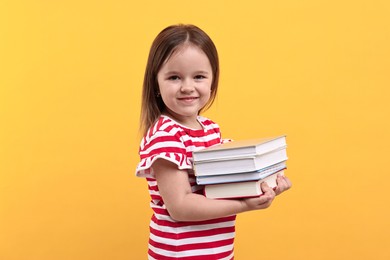 Photo of Cute little girl with books against orange background