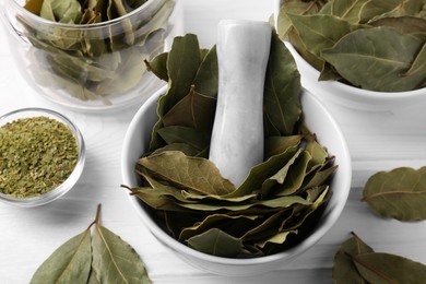 Photo of Whole and ground bay leaves on white wooden table, view from above