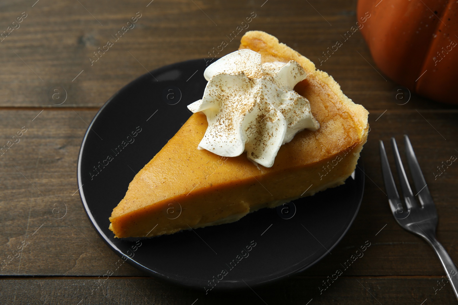 Photo of Piece of delicious pumpkin pie with whipped cream and fork on wooden table, closeup