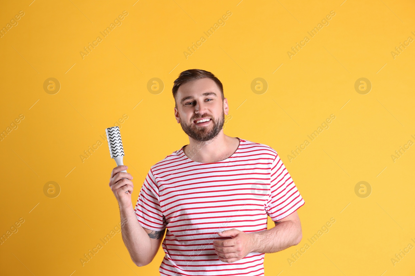 Photo of Young man cleaning clothes with lint roller on yellow background