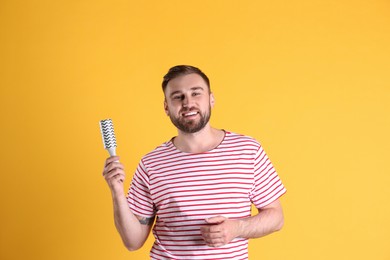 Photo of Young man cleaning clothes with lint roller on yellow background