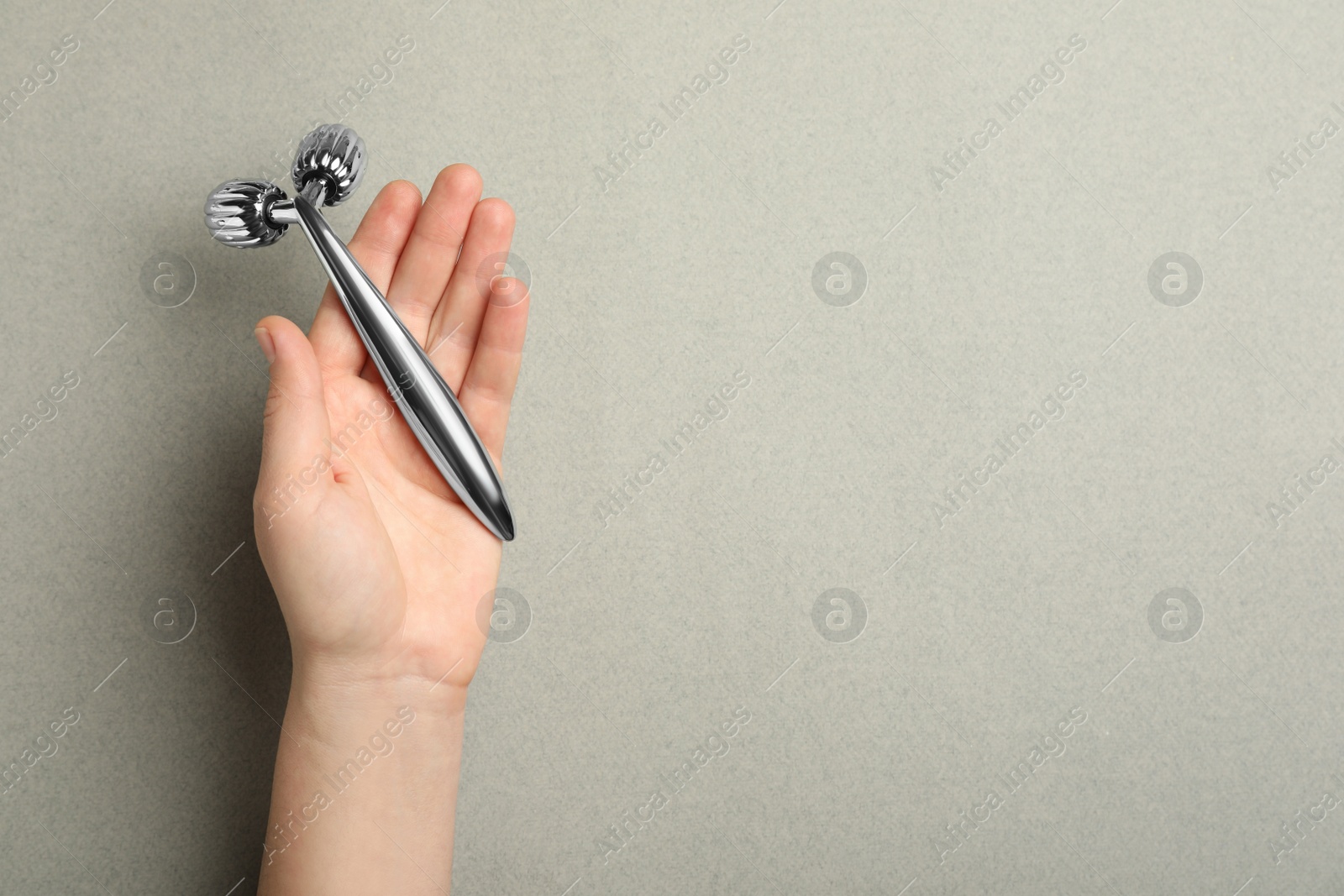 Photo of Woman with metal face roller on grey background, top view. Space for text