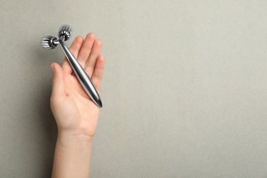 Woman with metal face roller on grey background, top view. Space for text