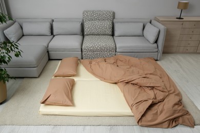 Photo of Mattress with pillows and blanket on floor near sofa. Additional sleep place for guest