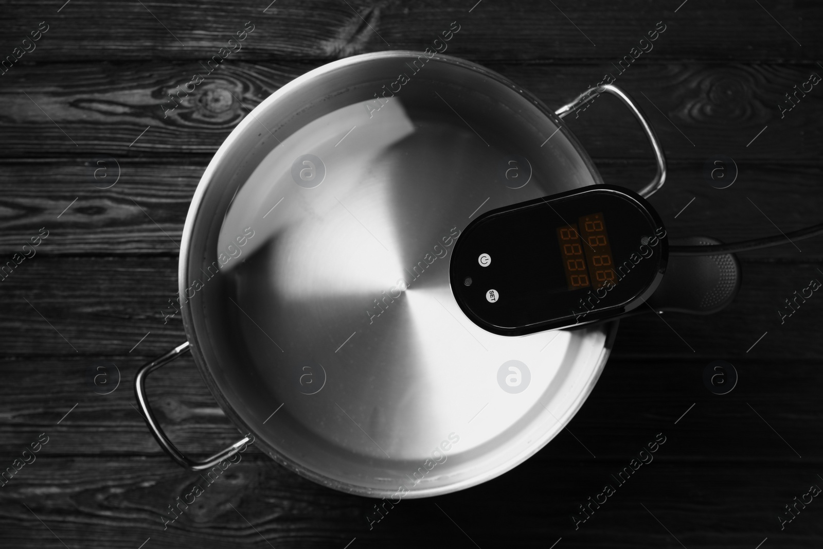 Photo of Thermal immersion circulator in pot on black wooden table, top view. Sous vide cooker