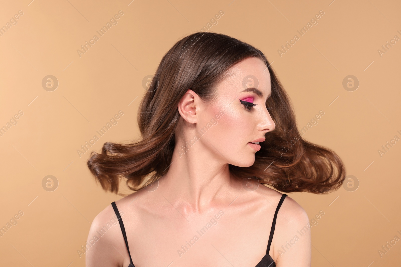 Photo of Portrait of beautiful young woman with makeup and gorgeous hair styling on beige background