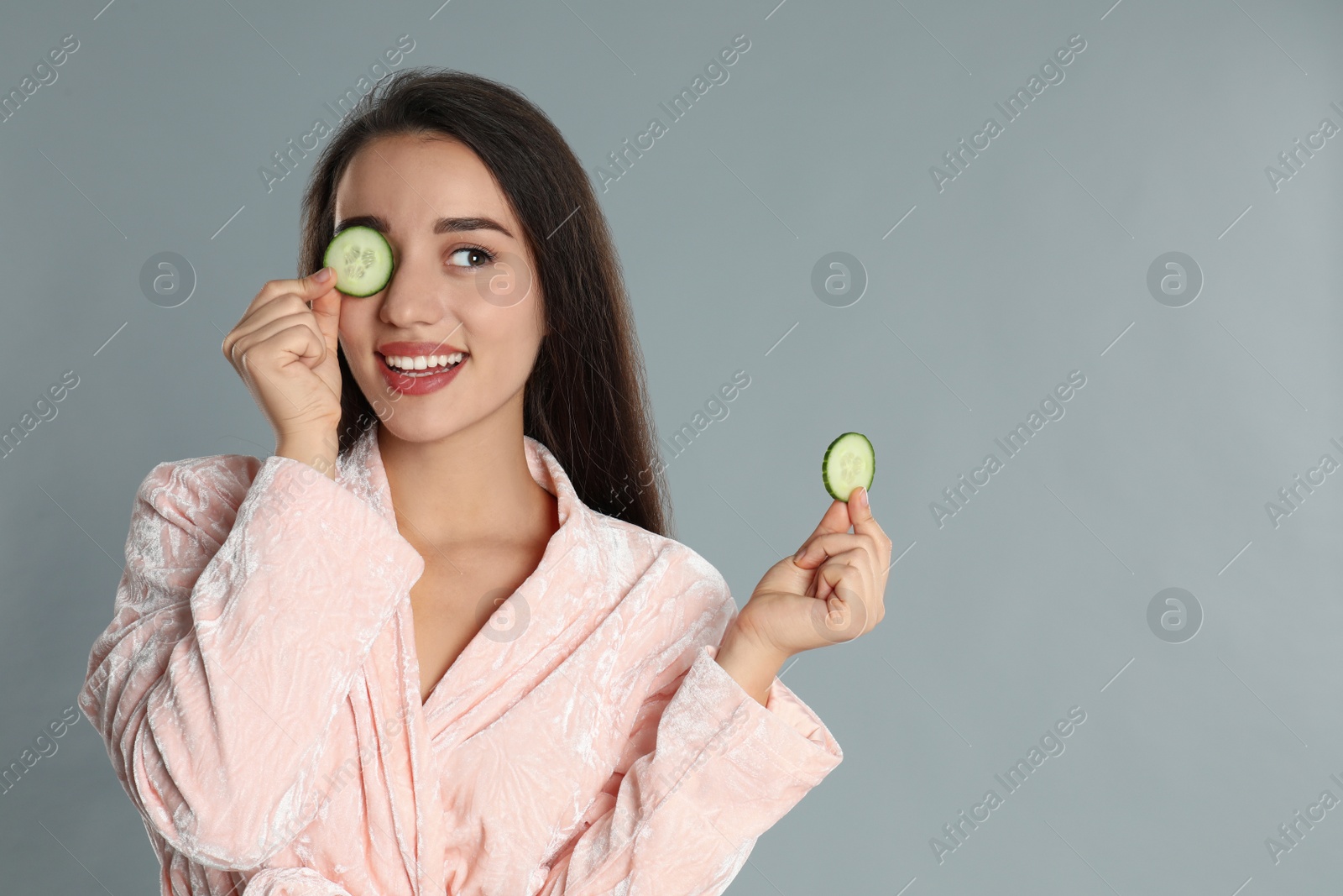 Photo of Young woman in bathrobe with cucumber slices on grey background
