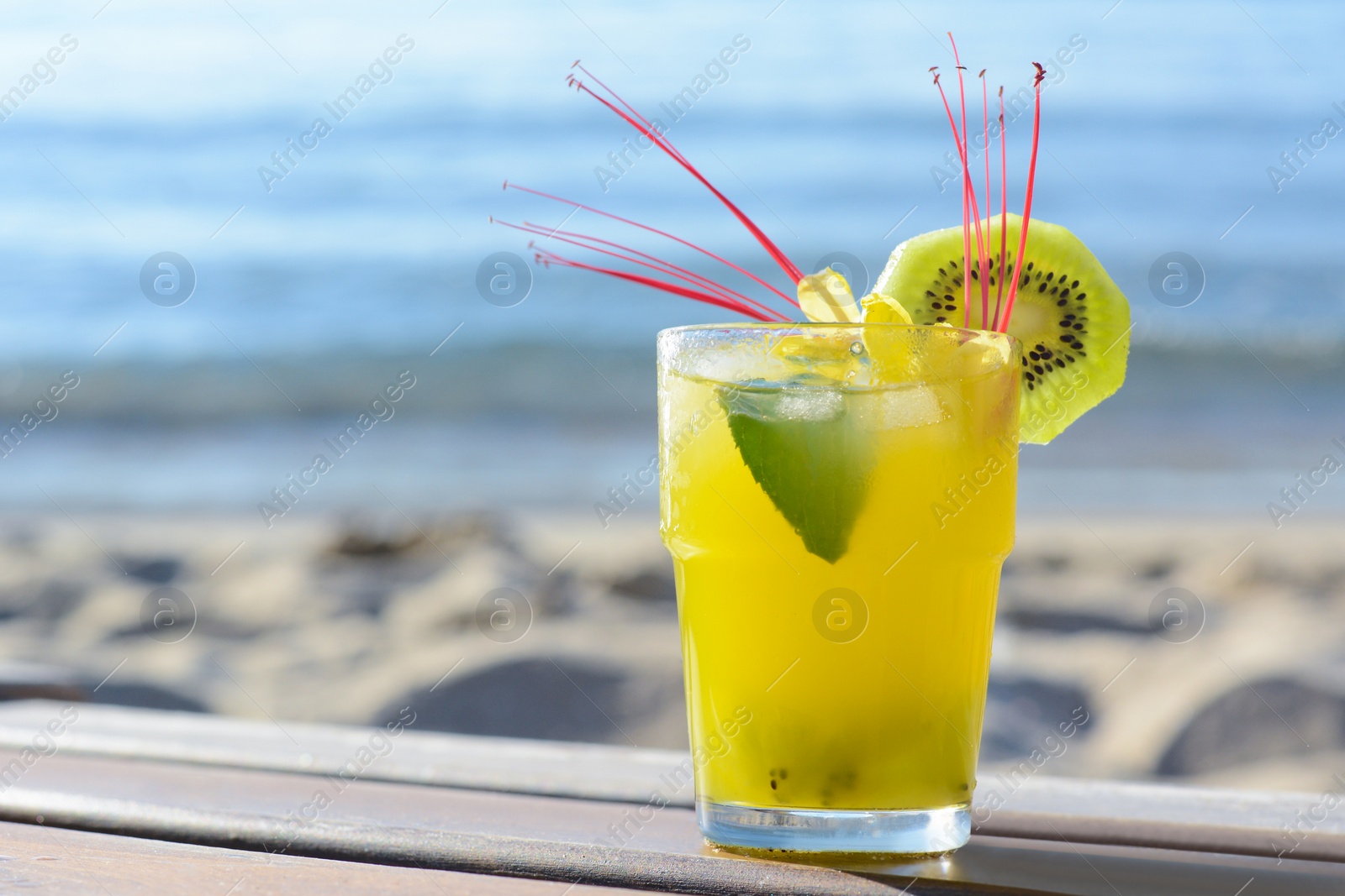 Photo of Glass of refreshing drink with kiwi and mint on wooden bench near sea. Space for text