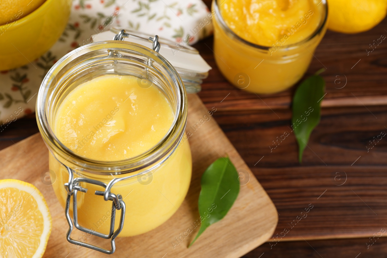 Photo of Delicious lemon curd in glass jars, fresh citrus fruit and green leaves on wooden table