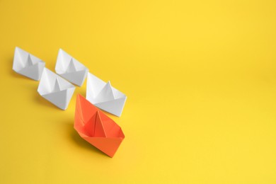 Group of paper boats following orange one on yellow background, space for text. Leadership concept