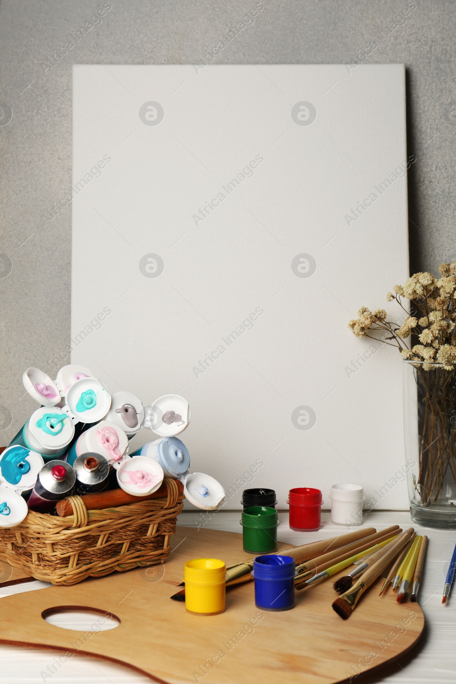 Photo of Blank canvas, paints and brushes on white wooden background