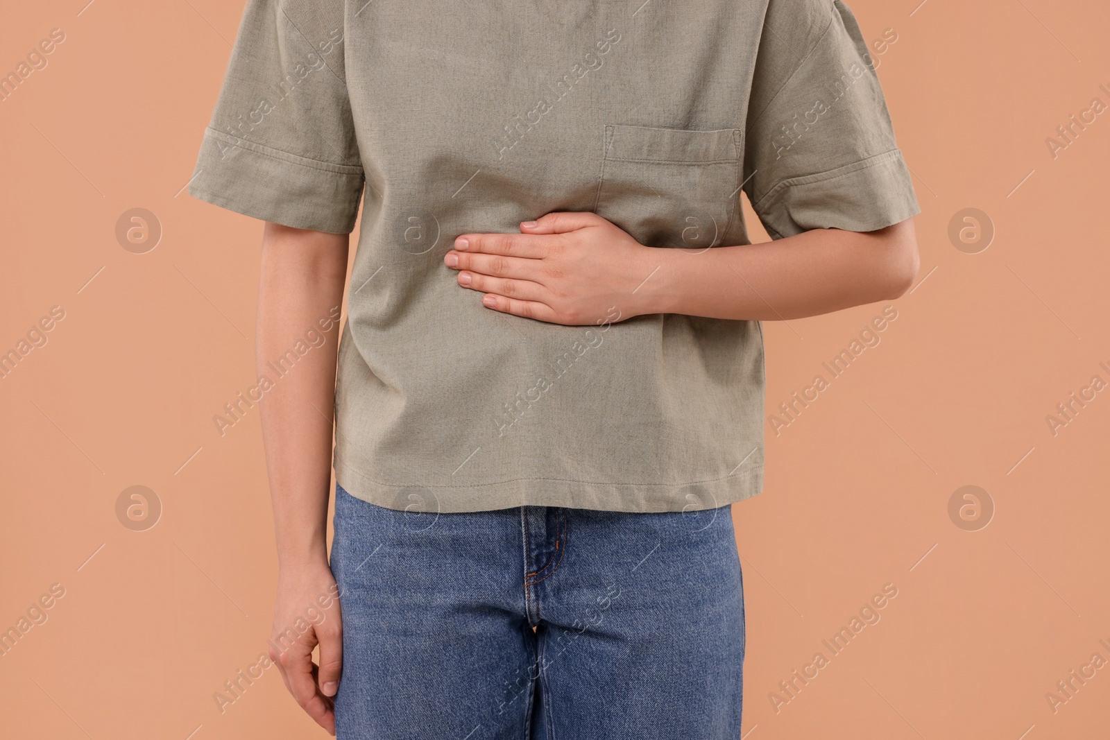 Photo of Woman suffering from abdominal pain on beige background, closeup. Unhealthy stomach