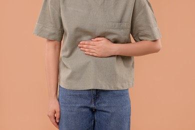 Photo of Woman suffering from abdominal pain on beige background, closeup. Unhealthy stomach