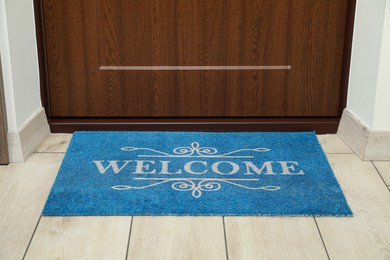 Photo of Beautiful blue doormat with word Welcome on floor near entrance