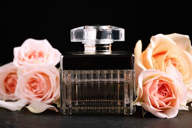 Photo of Bottle of perfume and beautiful roses on black table