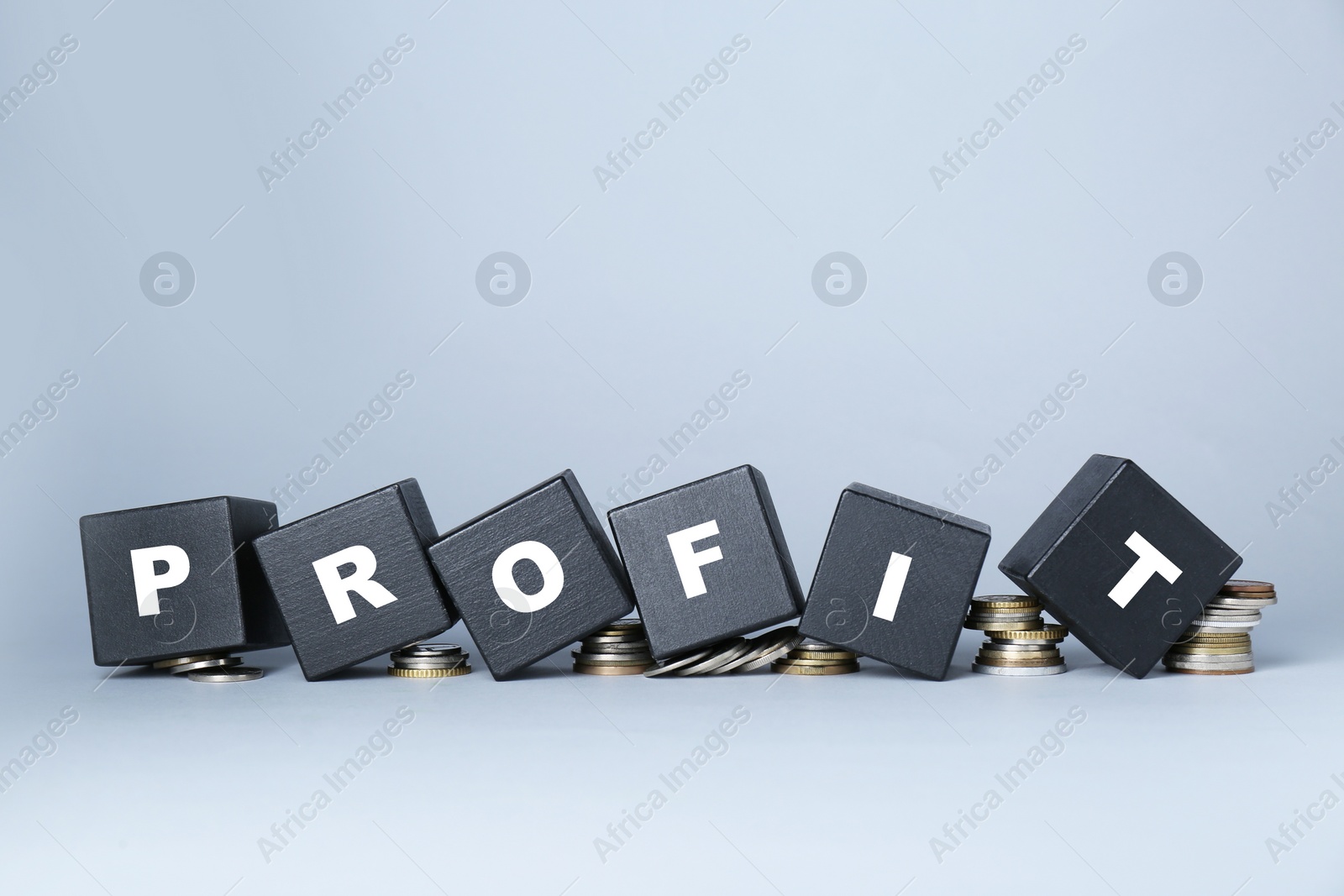 Photo of Black wooden cubes with word Profit and coins on light grey background