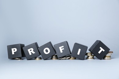 Photo of Black wooden cubes with word Profit and coins on light grey background