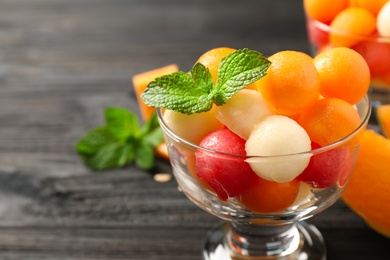 Photo of Melon and watermelon balls with mint in dessert bowl on black wooden table, closeup. Space for text
