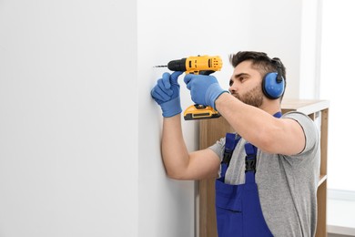 Young worker in uniform using electric drill indoors