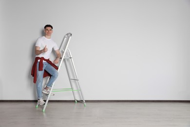 Photo of Handyman climbing up stepladder near white wall indoors. Space for text