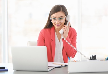 Photo of Young woman talking on phone at workplace