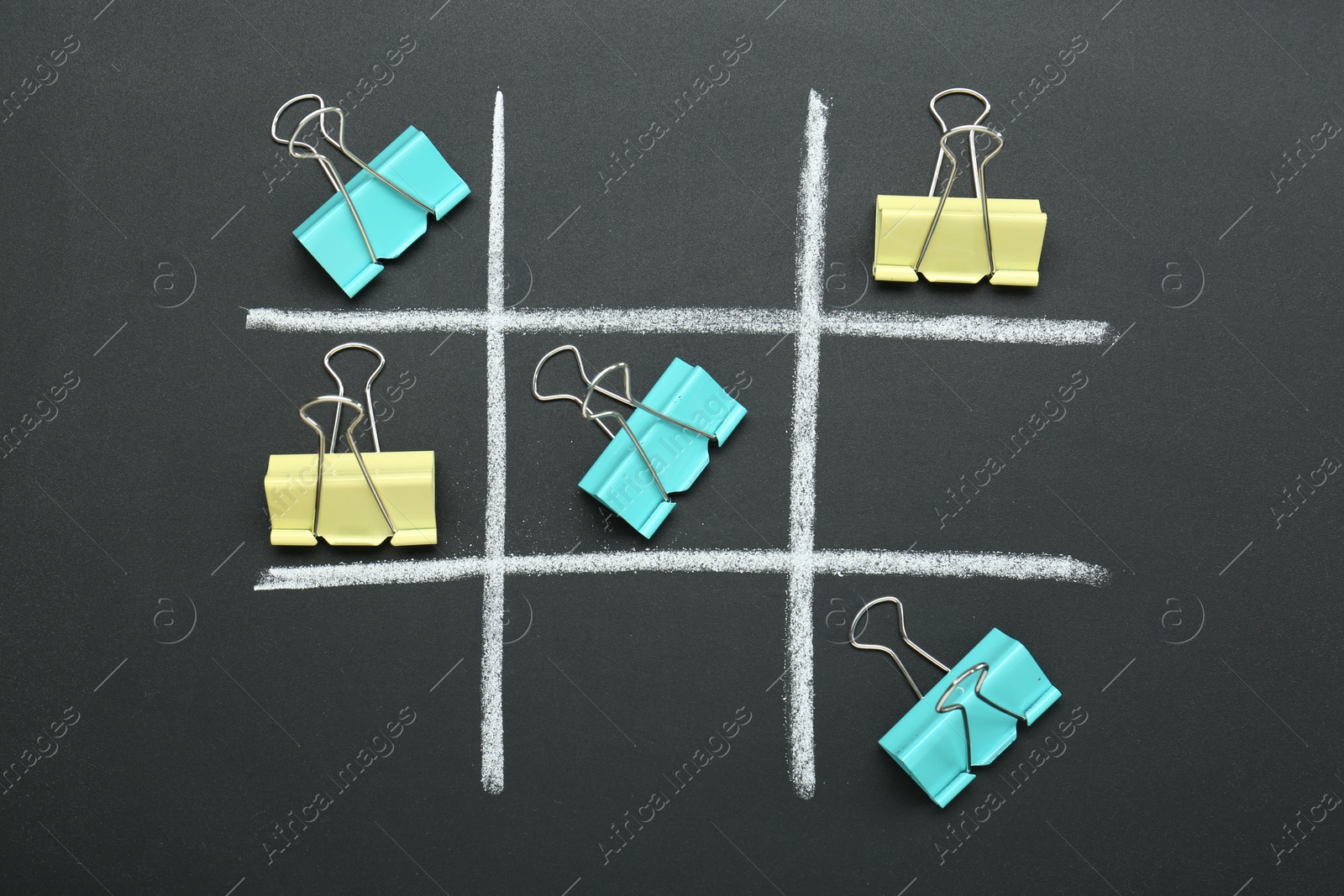 Photo of Tic tac toe game made with paper clips on chalkboard, top view