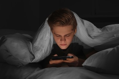 Teenage boy using smartphone under blanket on bed at night. Internet addiction