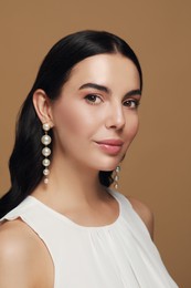 Photo of Young woman wearing elegant pearl earrings on brown background