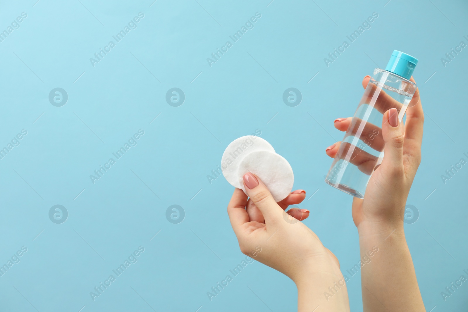 Photo of Woman holding makeup remover and cotton pads on light blue background, closeup. Space for text