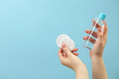 Photo of Woman holding makeup remover and cotton pads on light blue background, closeup. Space for text