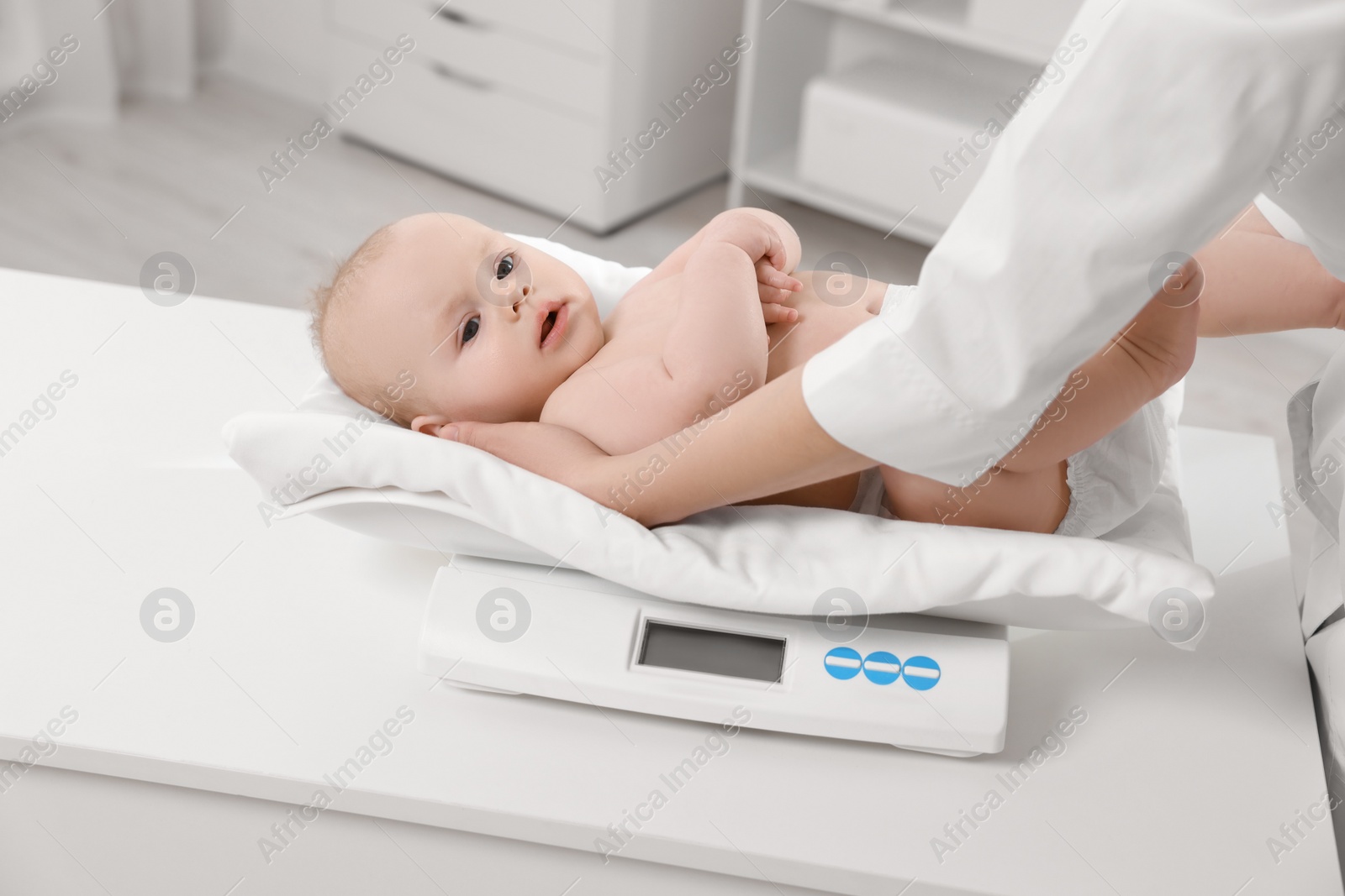 Photo of Pediatrician weighting cute little baby in clinic, closeup