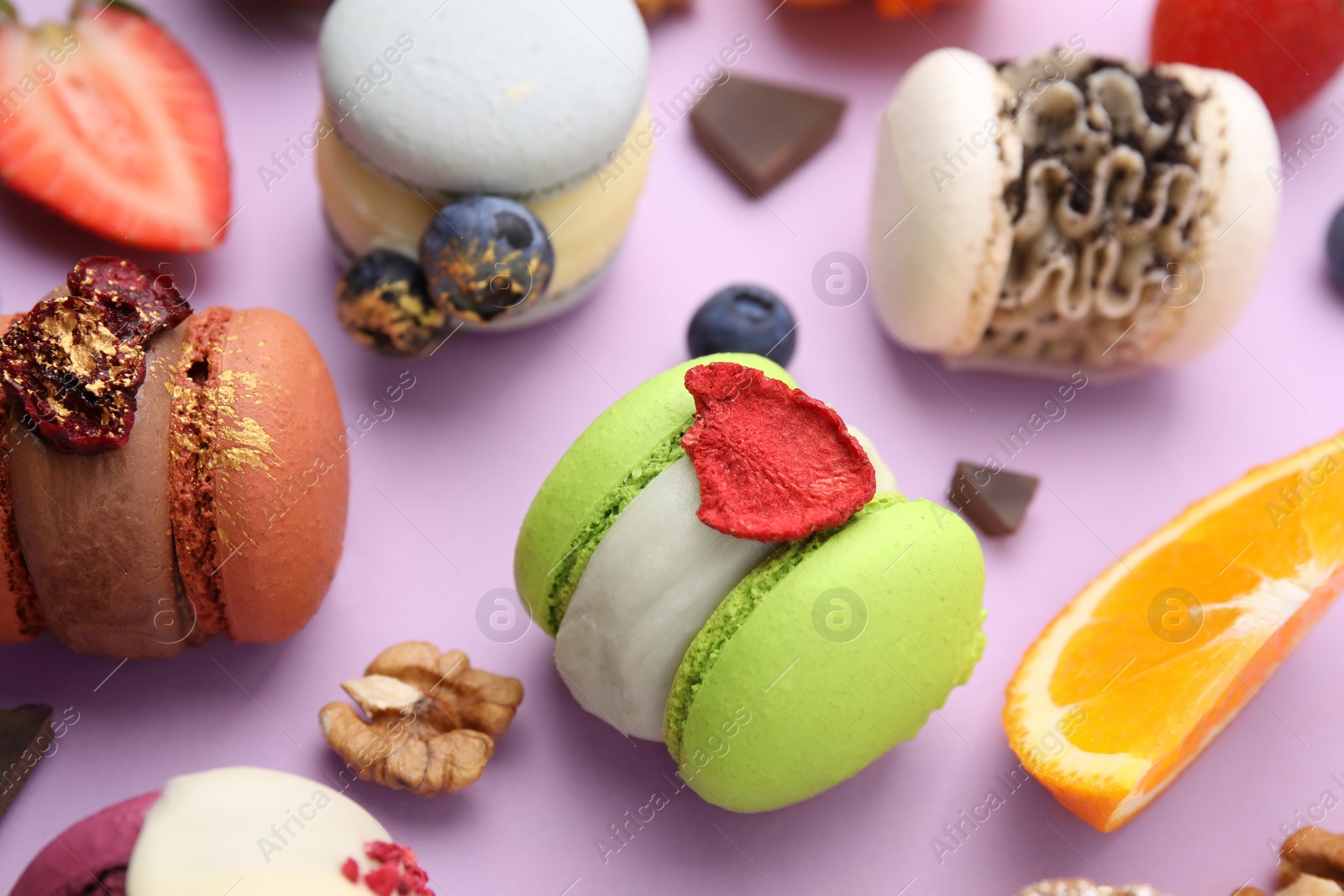 Photo of Delicious macarons, orange and berries on violet table, closeup